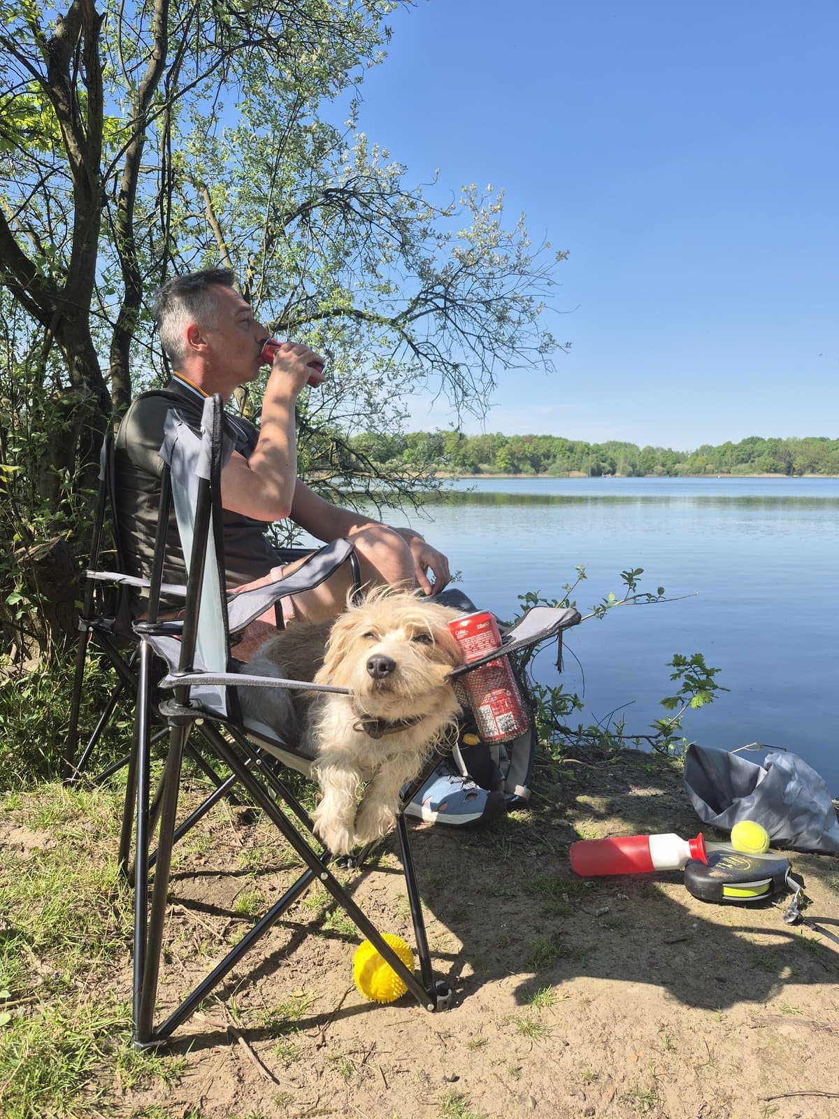 Prizeli's owner and dog beside a lake. The owner drinks from a can, not the mug.